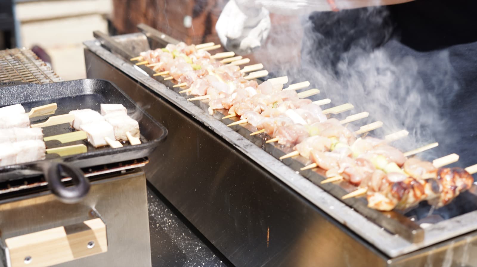 Yakitori skewers and pork belly grilling over binchotan with rising smoke