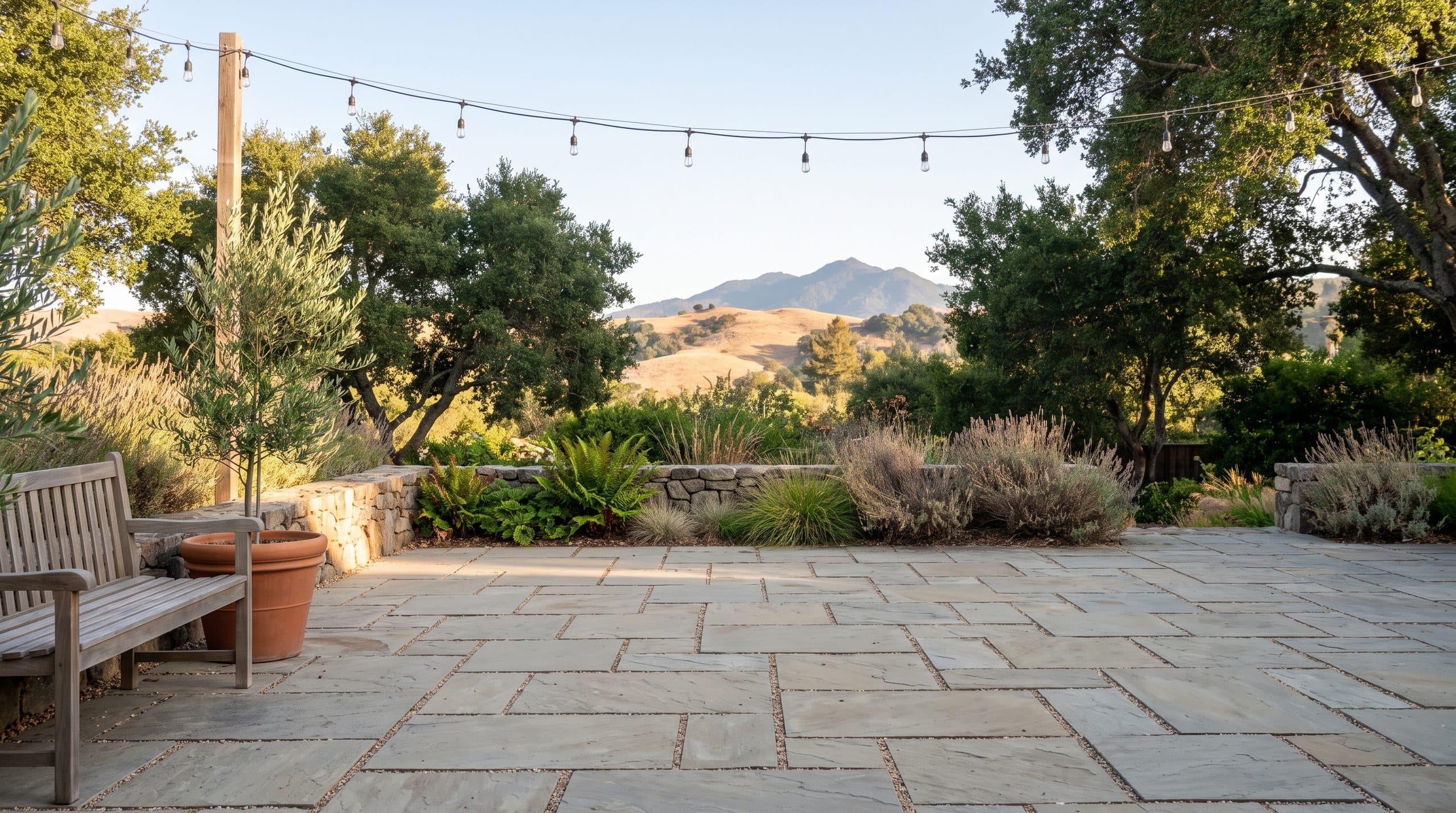 An empty flagstone patio in a Marin garden in the afternoon, under string lights, with Mount Tamalpais beyond