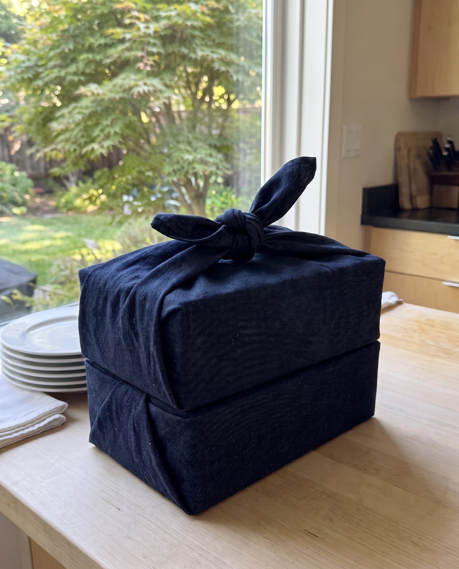A meal delivery wrapped in indigo denim and knotted on top, on a kitchen counter by a garden window