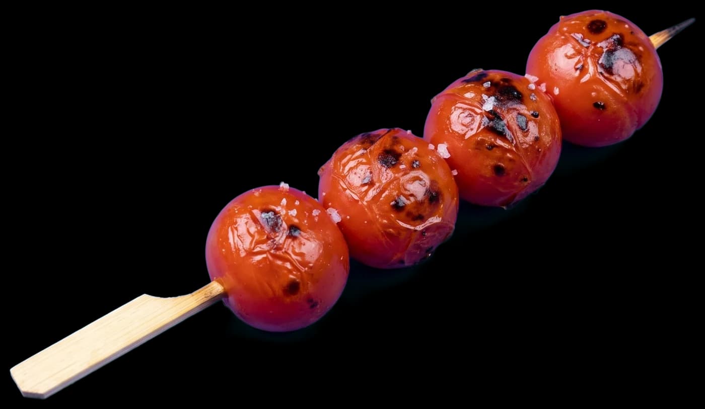 A cherry tomato skewer: four tomatoes, blistered and charred in spots, with flakes of salt
