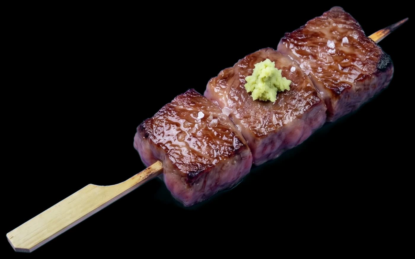 An A5 wagyu skewer: three seared, marbled cubes of beef with flakes of salt and a little fresh wasabi