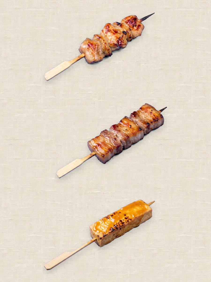 A chicken thigh skewer, a pork belly skewer and a tofu dengaku skewer on linen
